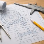 A detailed engineering blueprint with drafting tools, including a compass and caliper, on a wooden surface.